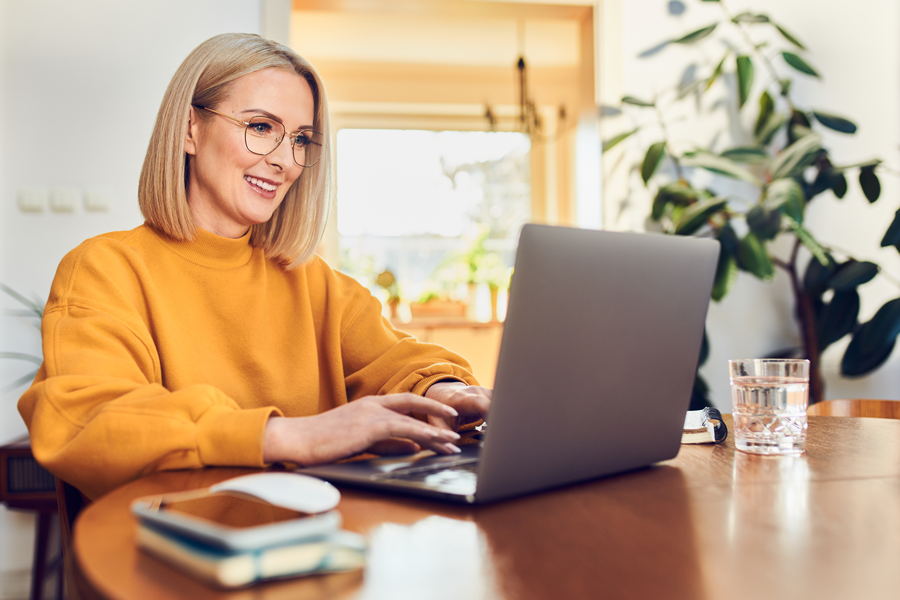 Woman in a yellow sweater works from home using a laptop.
