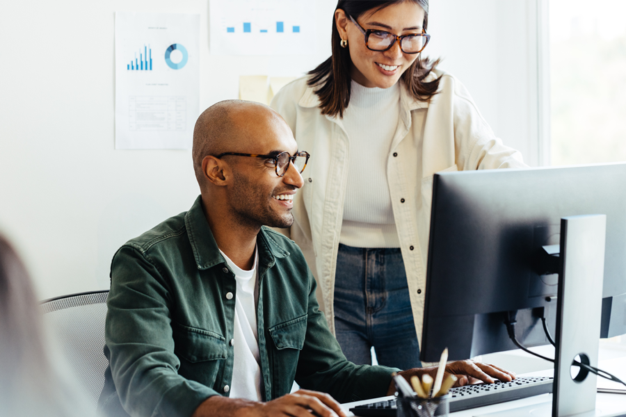Man and woman work together at a desktop computer at an office.